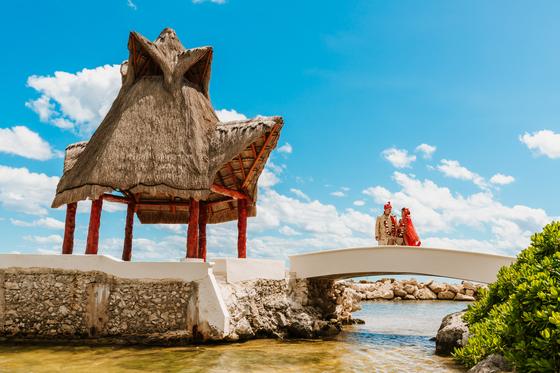 Couple small beneath the palapa against open sky