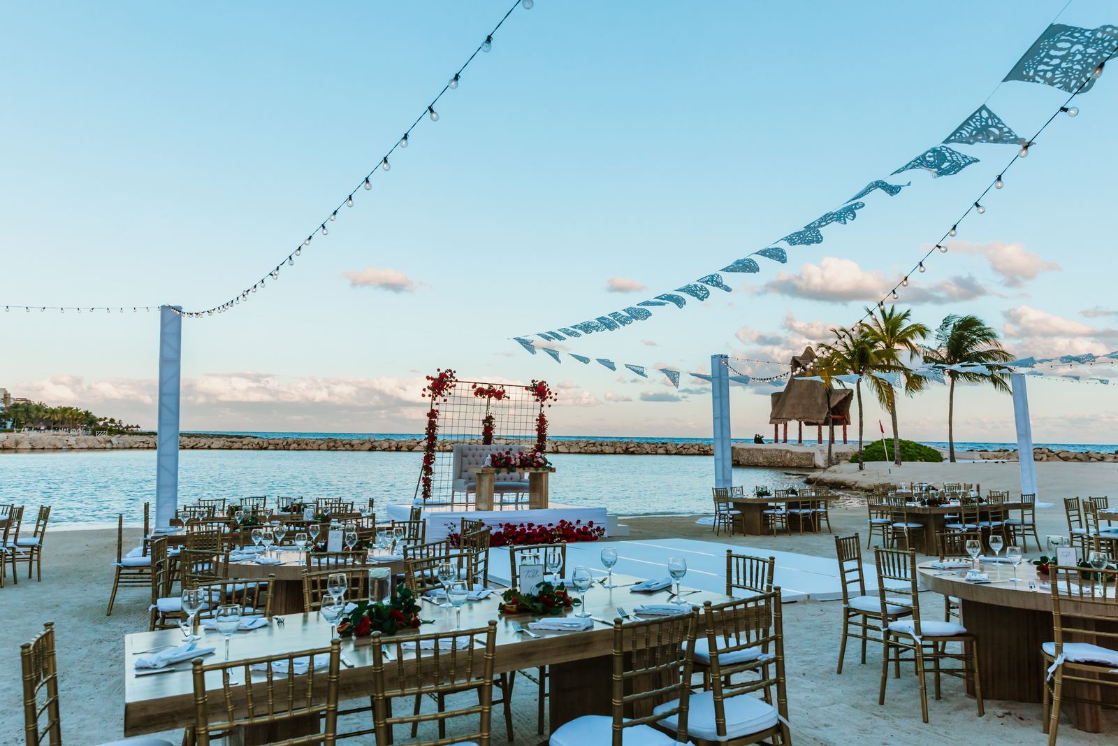 Reception tables on the sand at sunset under papel picado