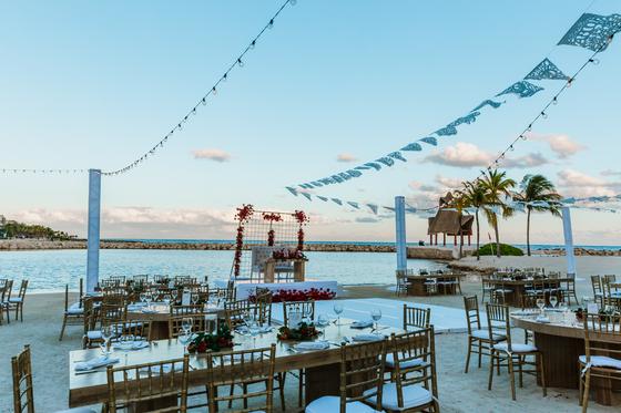 Reception tables on the sand at sunset under papel picado