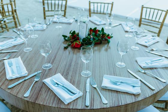 Round table set with linen, glassware and a rose centrepiece