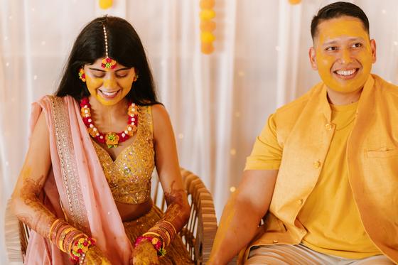 Couple seated together, covered in turmeric, laughing
