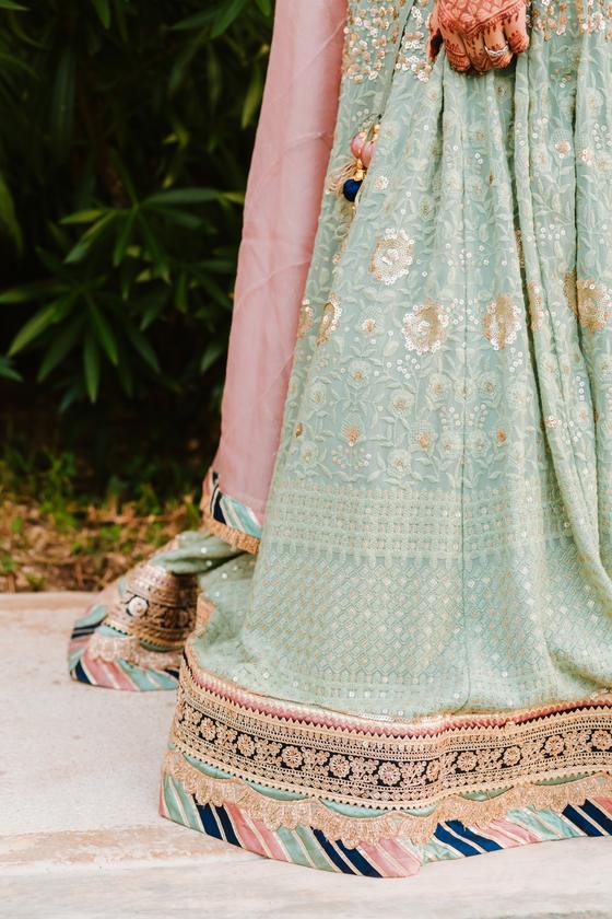 Embroidered hem of a mint lehenga against the pavement