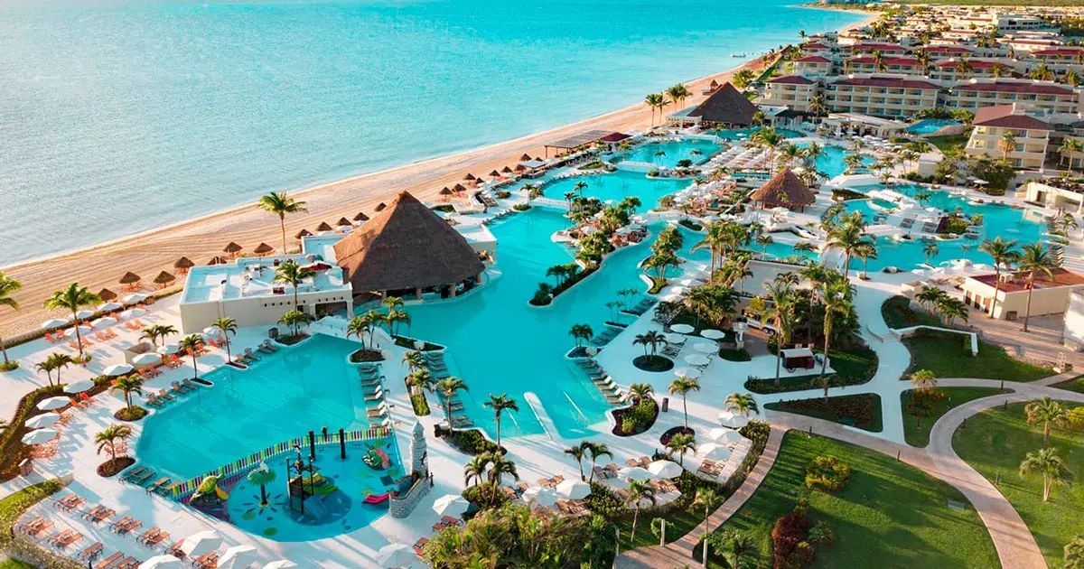 Aerial view of a large beachfront resort, its pools running down to the sand
