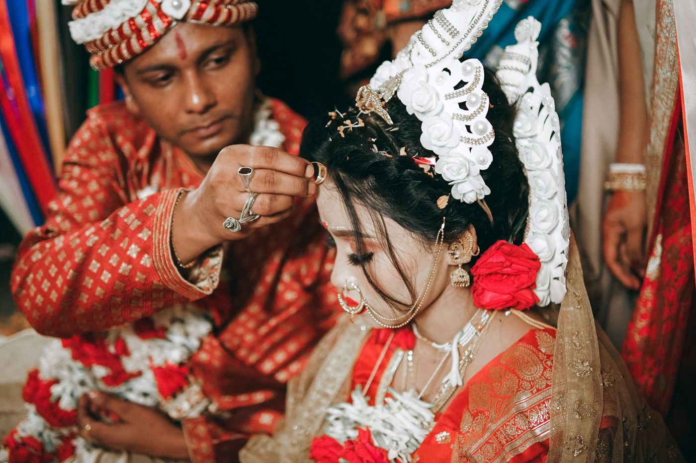 The groom applying sindoor to a bride in a white shola mukut