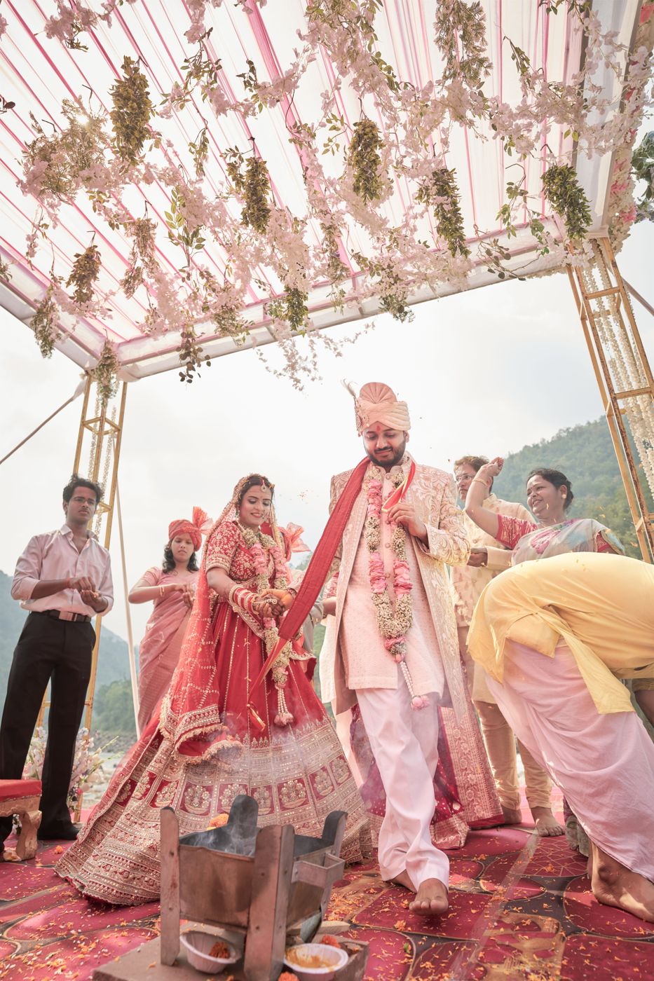 A couple circling the sacred fire under a floral mandap as family shower petals